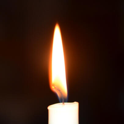 a white candle with a yellow flame against a dark background
